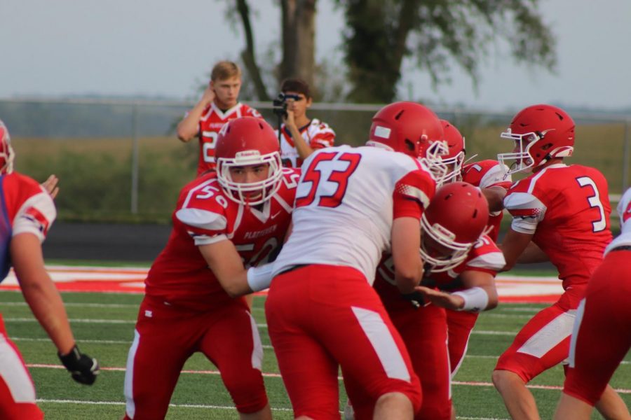 Senior Cade Demro hands the ball off to fellow senior Tobius Nixon on Friday, August 23 for the Red & White scrimmage on Salberg Field while seniors Grant Mitchell and Byron Ehrke block junior Brennan Campbell. In the back, freshmen Ethan Golda and Bryar Nadrchal take video for the football team to scrutinize after the game.